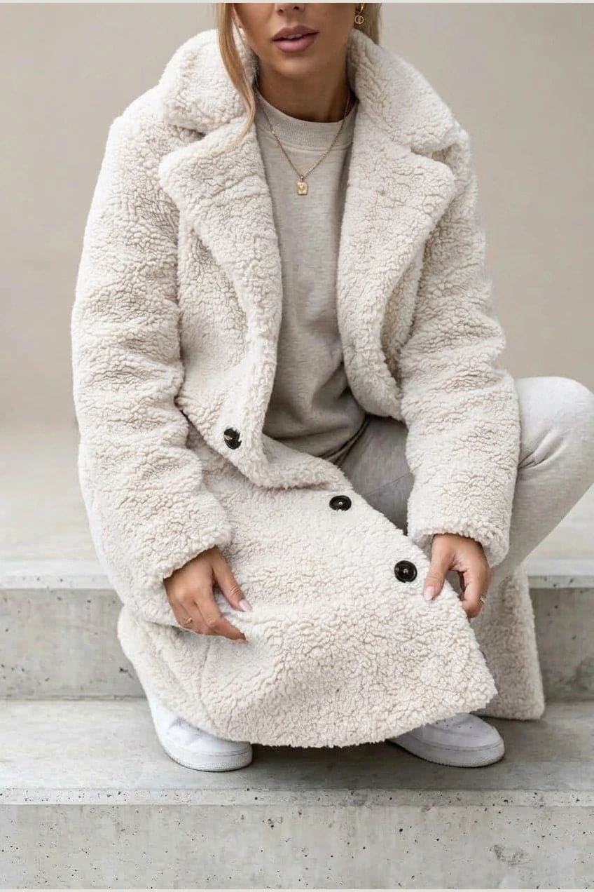 Woman wearing a long textured teddy coat with notch lapels and button front, open over a jumper and trousers with ankle boots._4