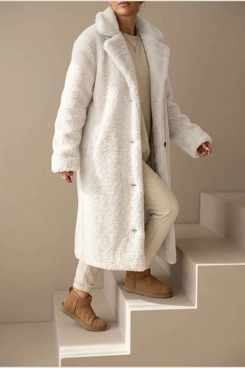 Woman wearing a long textured teddy coat with notch lapels and button front, open over a jumper and trousers with ankle boots._5