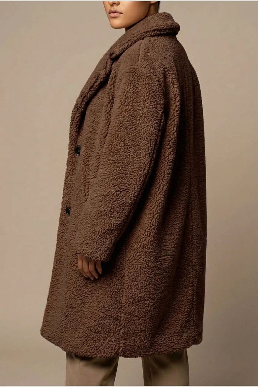 Woman wearing a long textured teddy coat with notch lapels and button front, open over a jumper and trousers with ankle boots._9