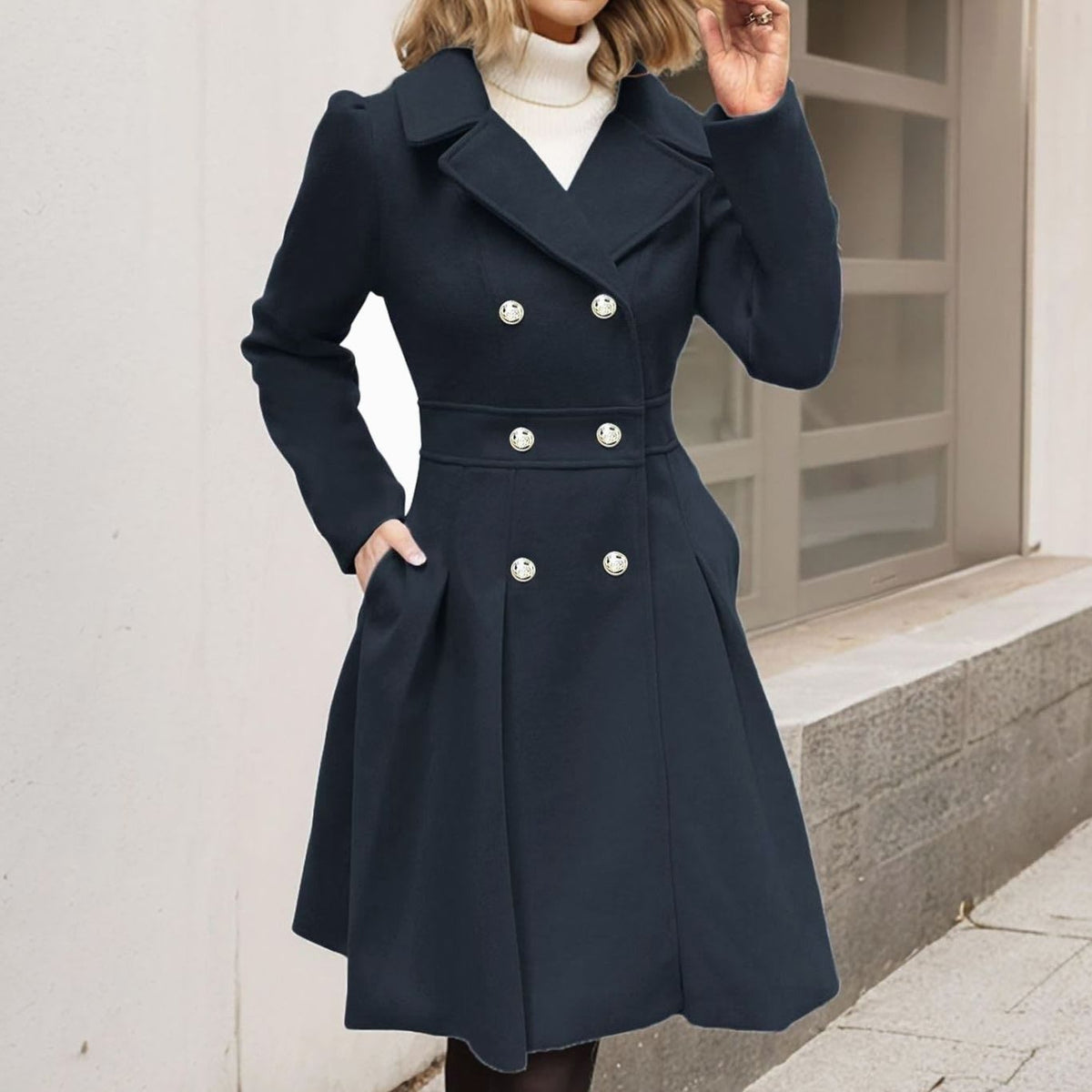Woman wearing a long double breasted coat with notch lapels, decorative buttons, a defined waist seam and a pleated flared skirt._0
