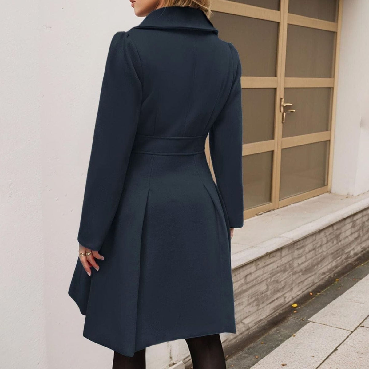 Woman wearing a long double breasted coat with notch lapels, decorative buttons, a defined waist seam and a pleated flared skirt._1