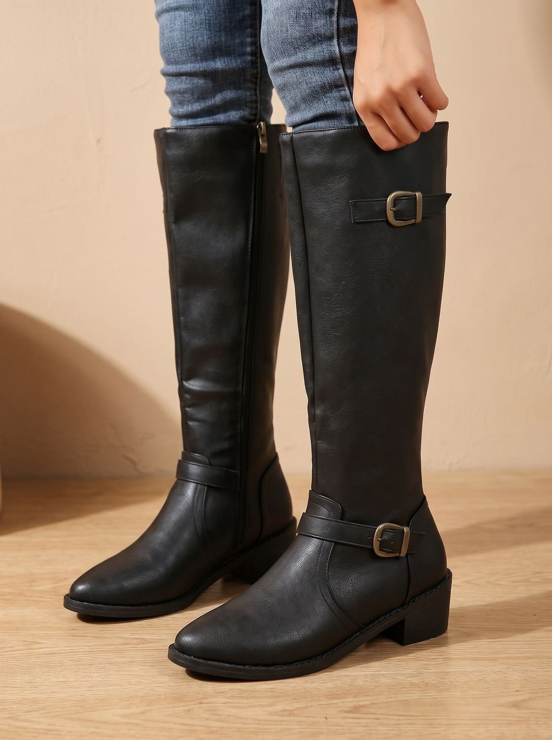 Black knee-high boots standing side by side, clearly showing the tall shafts, side zips, paired buckles, and low block heels.