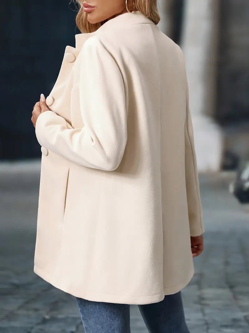 Woman wearing a hip-length stand collar coat with front buttons and side pockets, over a vest top and jeans._3