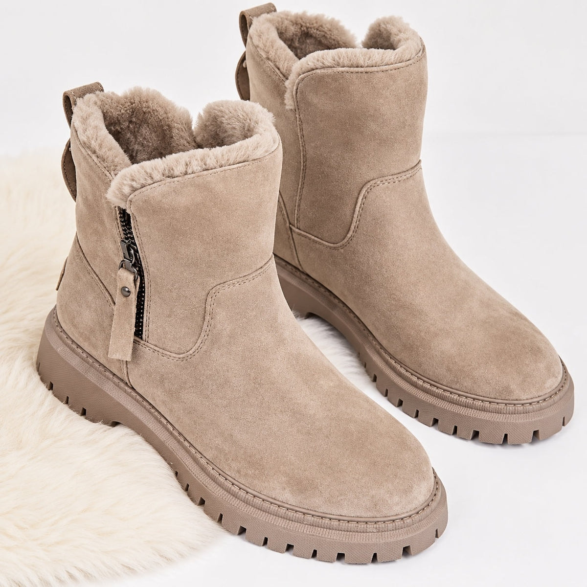 Taupe ankle boots displayed from an elevated front angle, showing the rounded toes, plush lining, side zips, and deep lug tread.