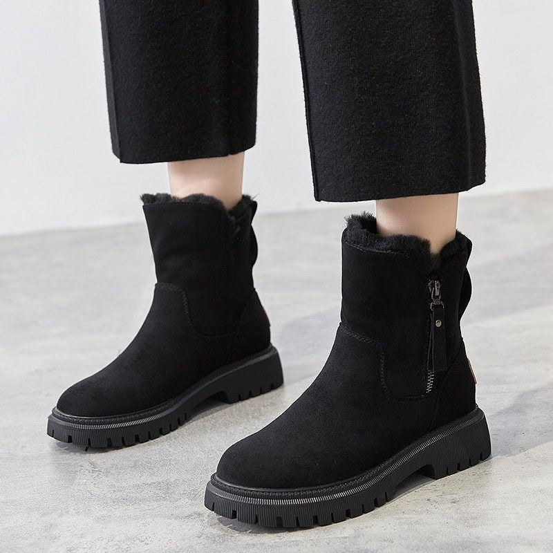 Black ankle boots worn with cropped trousers, showing their ankle height, faux fur trim, side zips, and chunky traction soles.