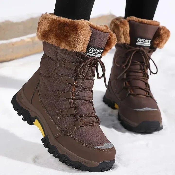 Pair of brown ankle-length winter boots with warm brown faux fur cuffs, matching laces, reinforced toe accents, and black lug soles shown against a snowy backdrop.