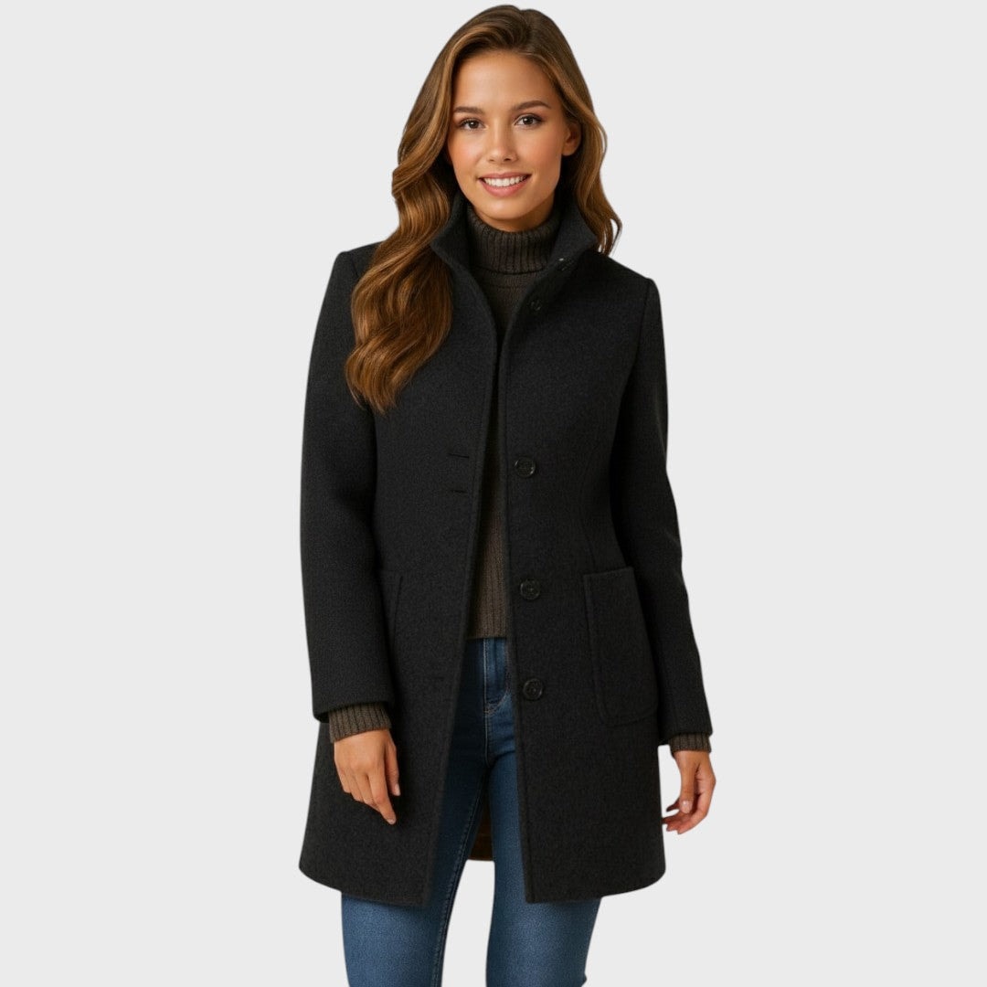 Front view of the black mid-length coat styled over a sweater, showing its raised collar, button front, and large patch pockets.