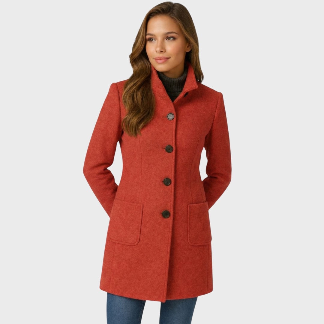 Three-quarter front view of the red fitted coat with its stand collar fastened, visible button closure, and hands resting in the patch pockets.