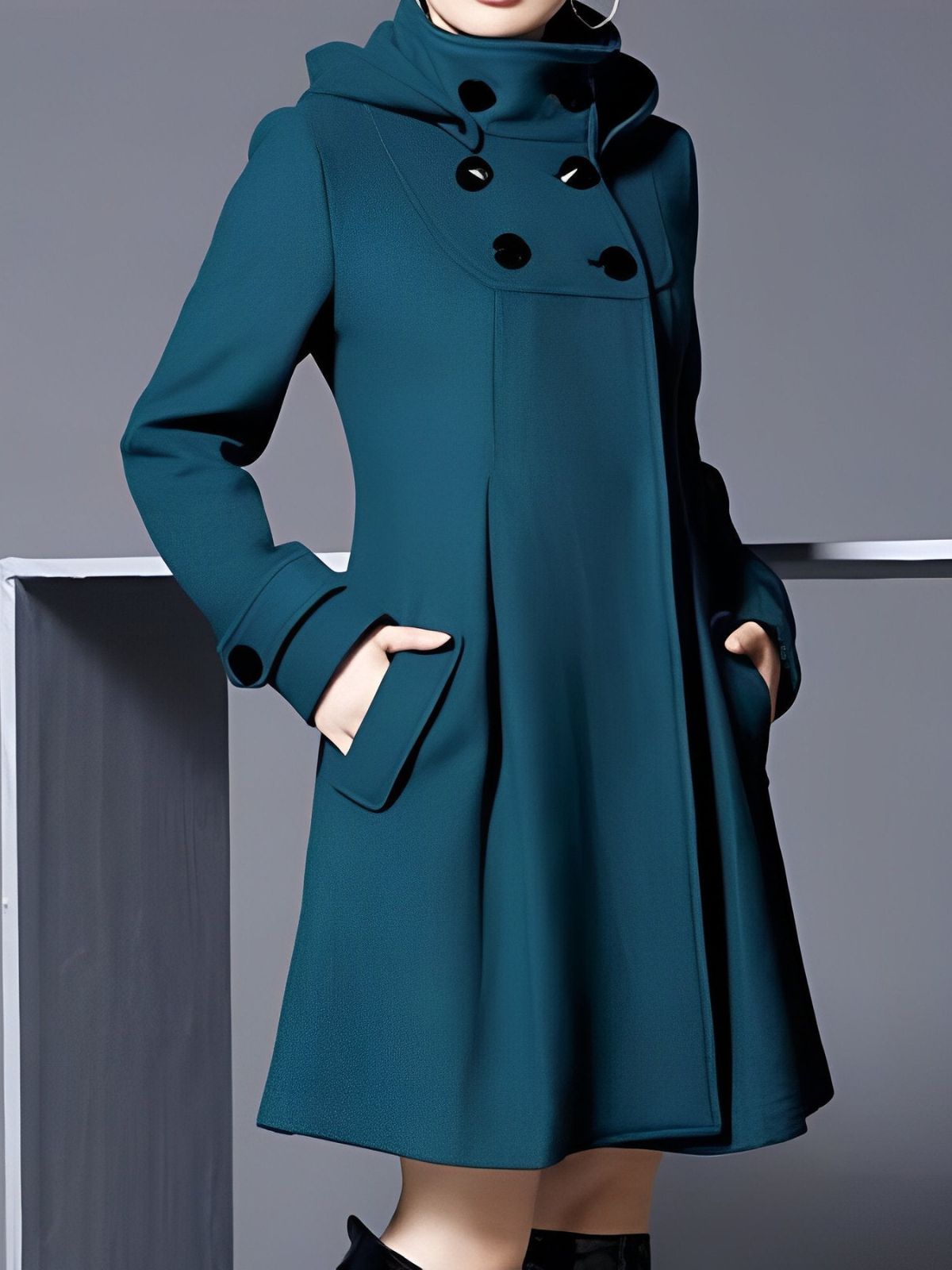 Full-length view of the teal hooded coat, showing its flared hem, long sleeves, and hands resting in the front pockets.