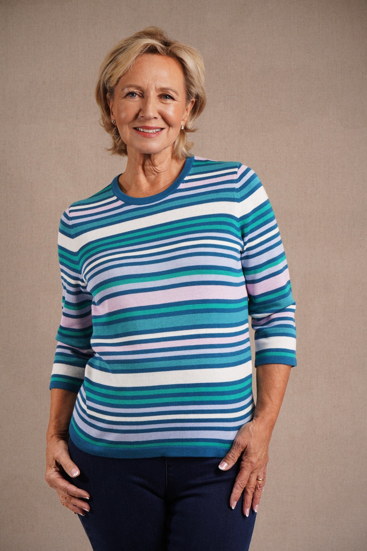 Woman wearing a multi striped three quarter sleeve crew neck knitted jumper with ribbed neckline, cuffs and hem, with dark trousers._0