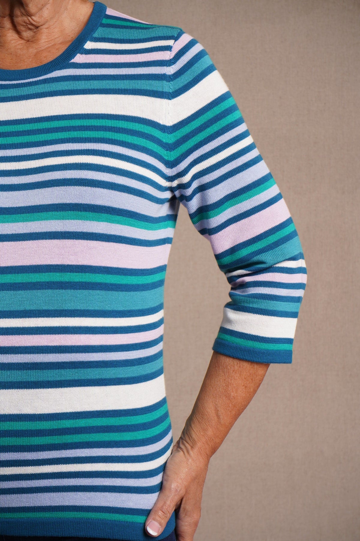 Woman wearing a multi striped three quarter sleeve crew neck knitted jumper with ribbed neckline, cuffs and hem, with dark trousers._11