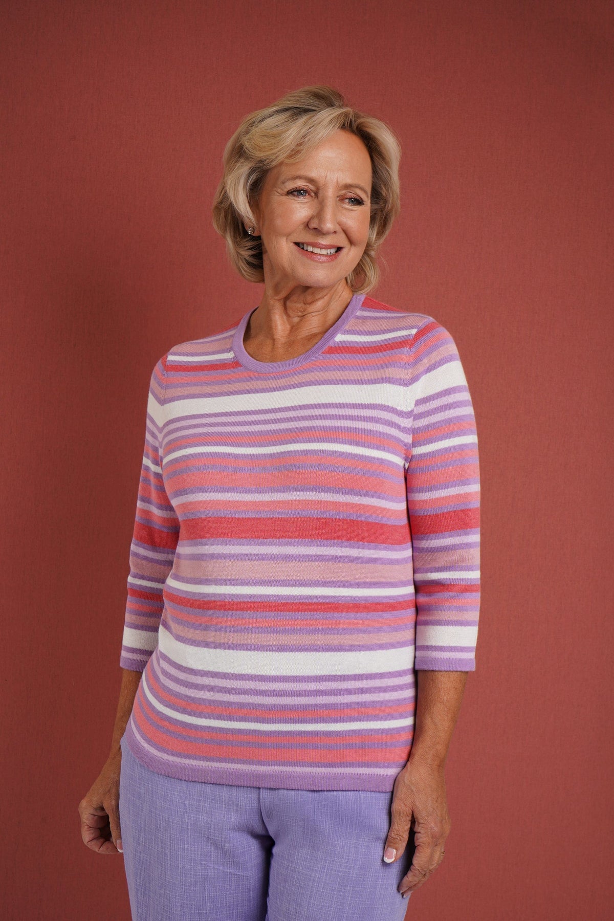 Woman wearing a multi striped three quarter sleeve crew neck knitted jumper with ribbed neckline, cuffs and hem, with dark trousers._2