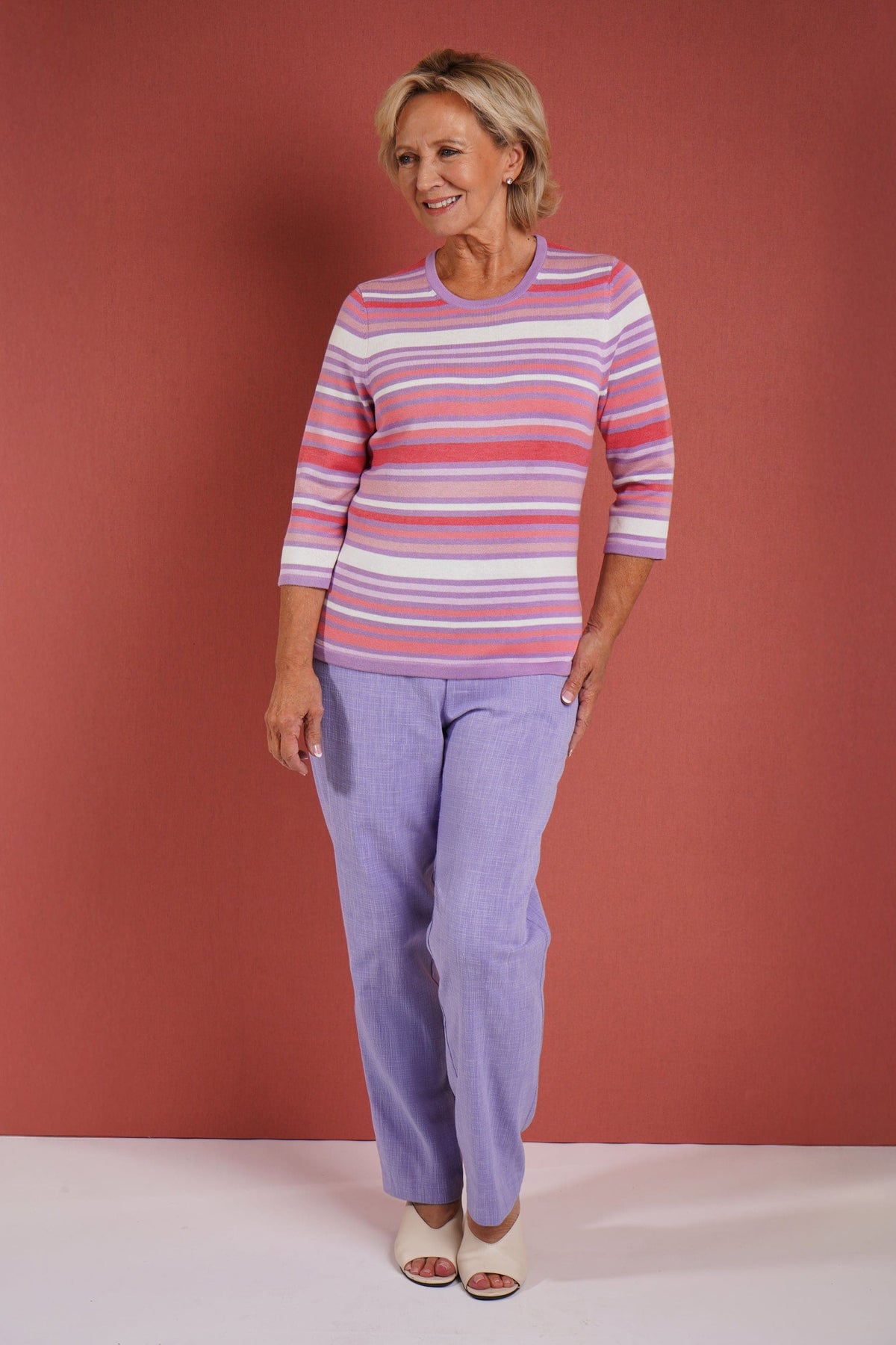 Woman wearing a multi striped three quarter sleeve crew neck knitted jumper with ribbed neckline, cuffs and hem, with dark trousers._3