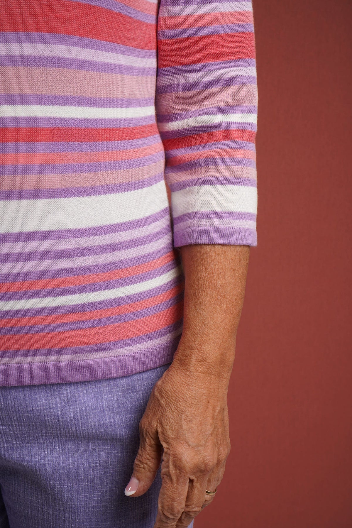 Woman wearing a multi striped three quarter sleeve crew neck knitted jumper with ribbed neckline, cuffs and hem, with dark trousers._6