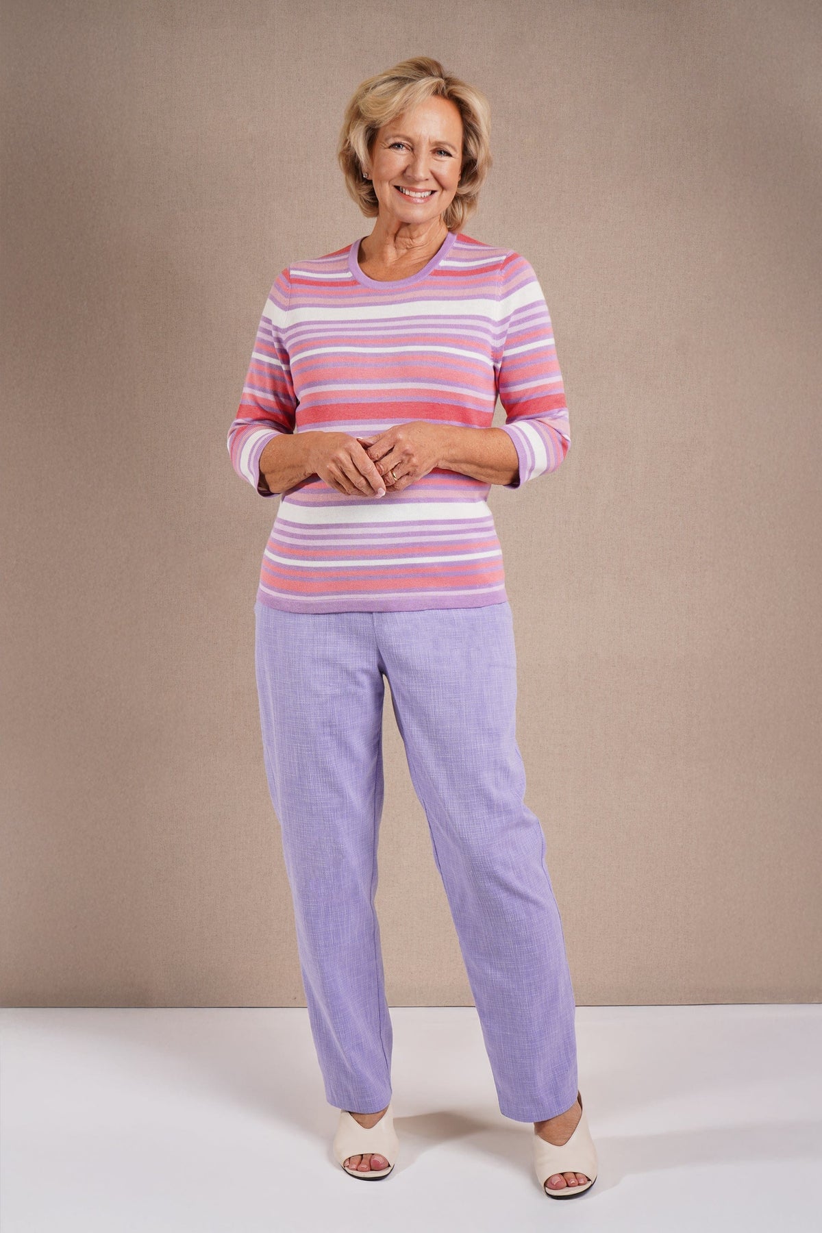 Woman wearing a multi striped three quarter sleeve crew neck knitted jumper with ribbed neckline, cuffs and hem, with dark trousers._7