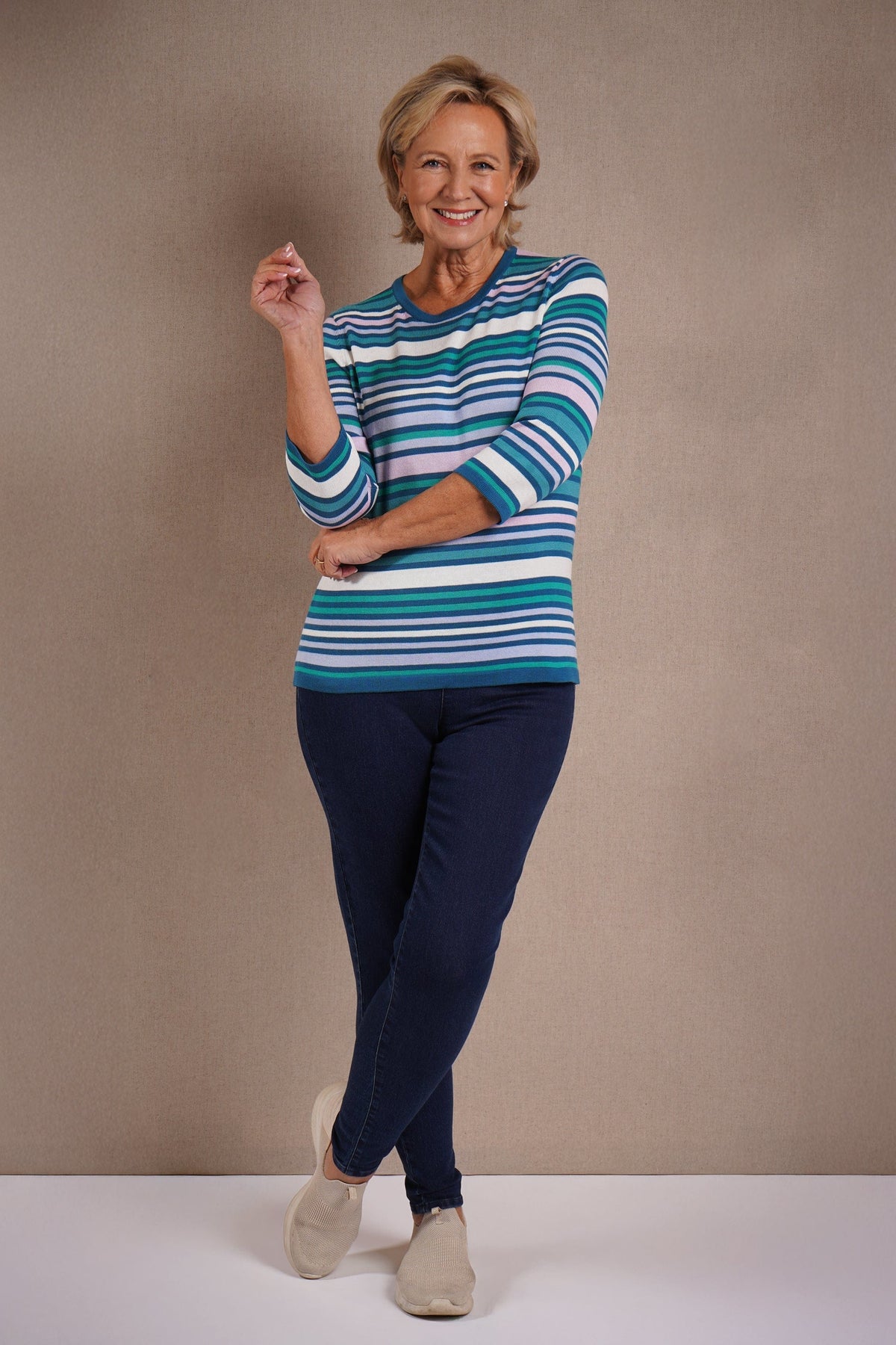 Woman wearing a multi striped three quarter sleeve crew neck knitted jumper with ribbed neckline, cuffs and hem, with dark trousers._8