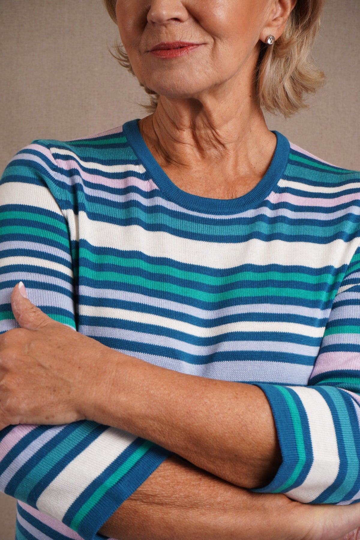 Woman wearing a multi striped three quarter sleeve crew neck knitted jumper with ribbed neckline, cuffs and hem, with dark trousers._9