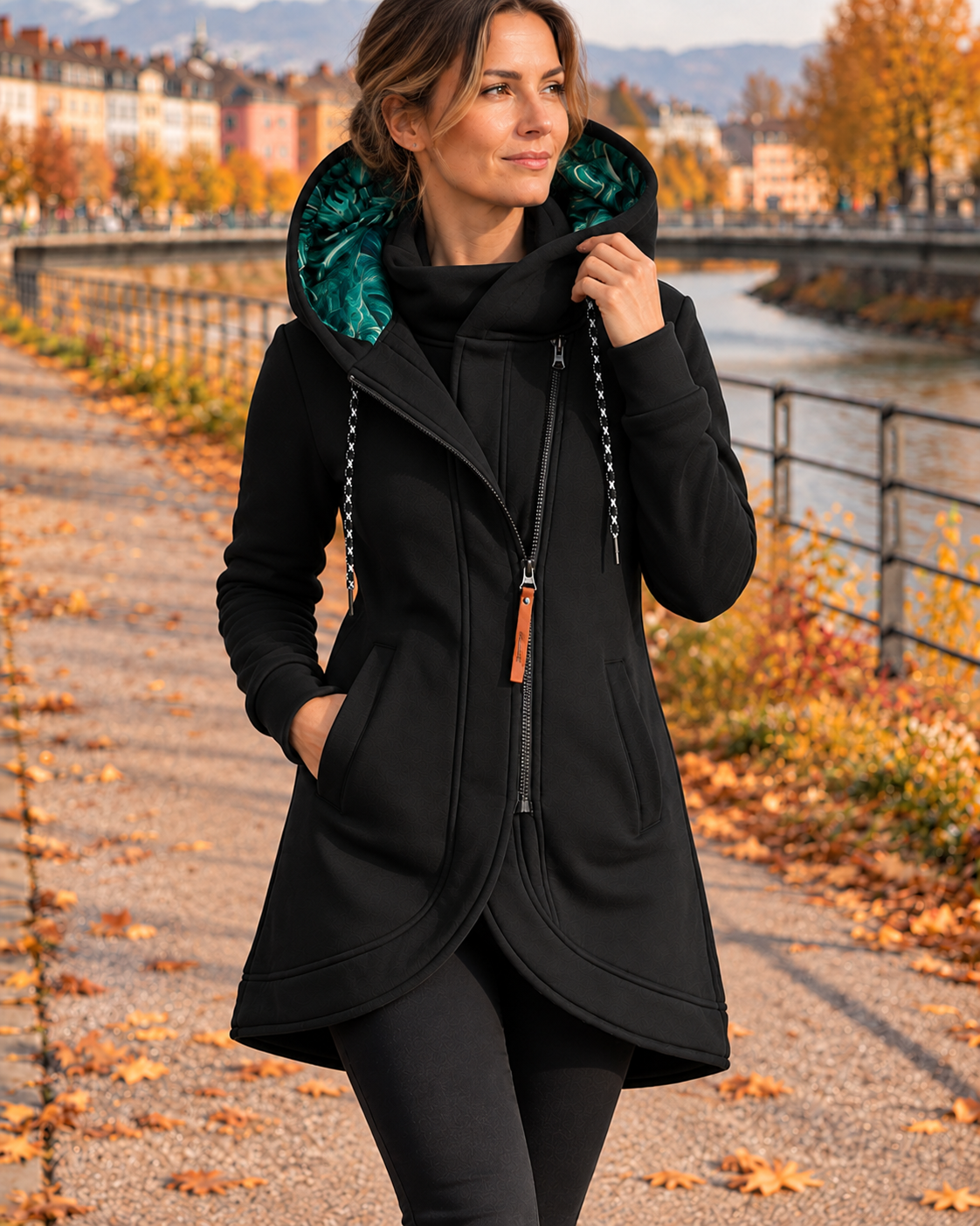 Black longline hooded jacket with teal-lined hood, diagonal zip fastening, drawcords, and hands placed in the side pockets.