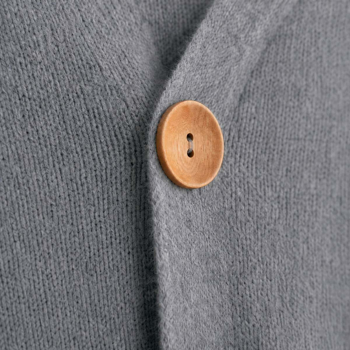 Close-up of a round wooden button fastening the gray cardigan.