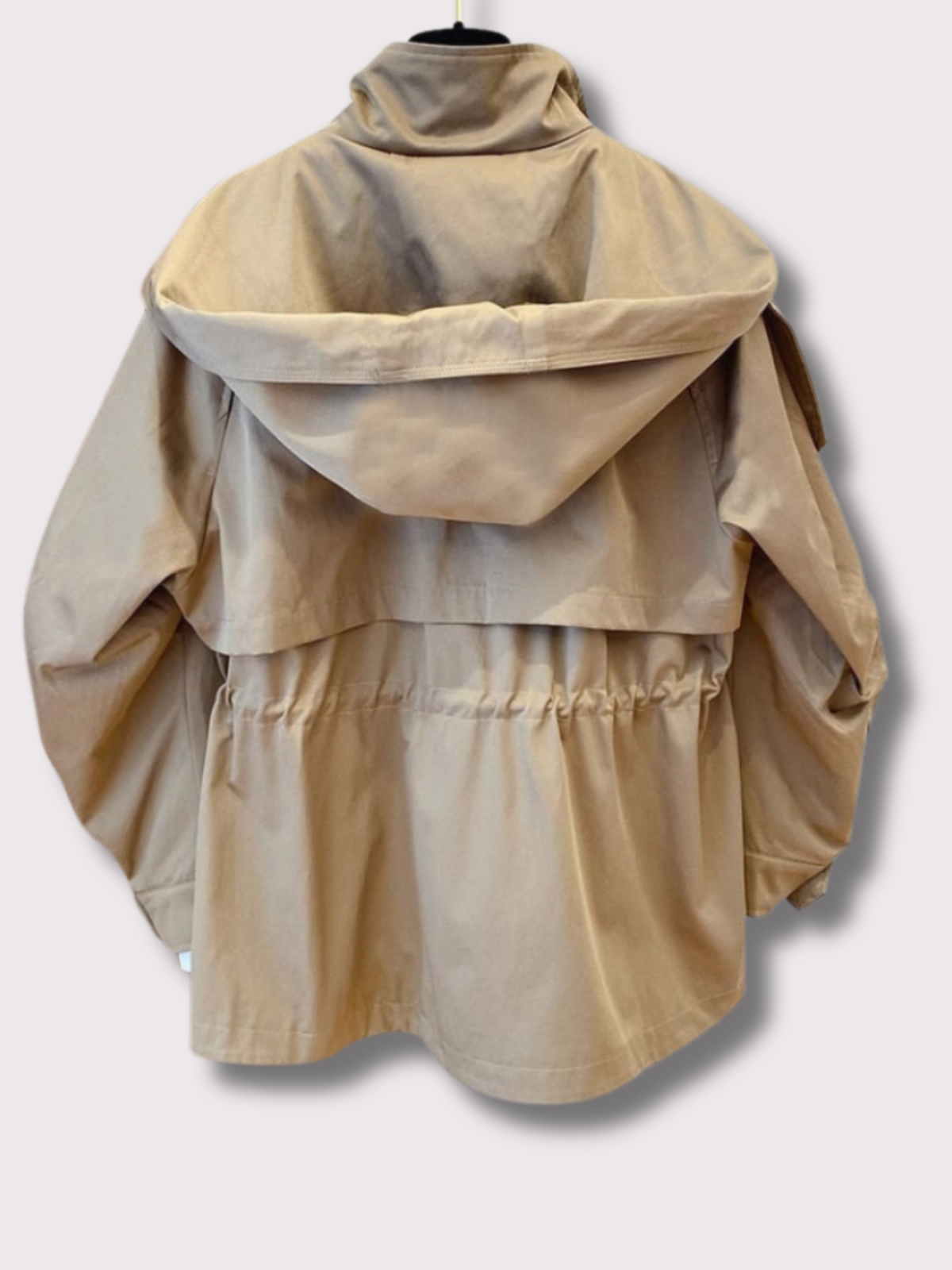 Back view of a beige hooded jacket showing the oversized hood, cape-like back panel, gathered drawstring waist, and loose sleeves.