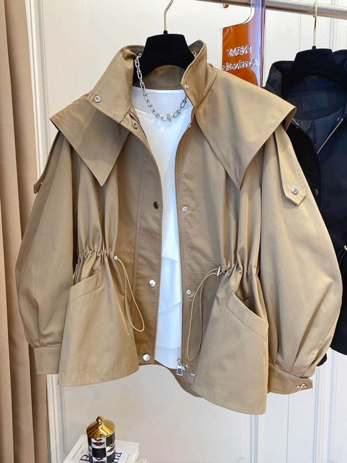Front view of the beige jacket styled over a white top, with a wide collar, full sleeves, front closure, waist drawstrings, and roomy pockets.