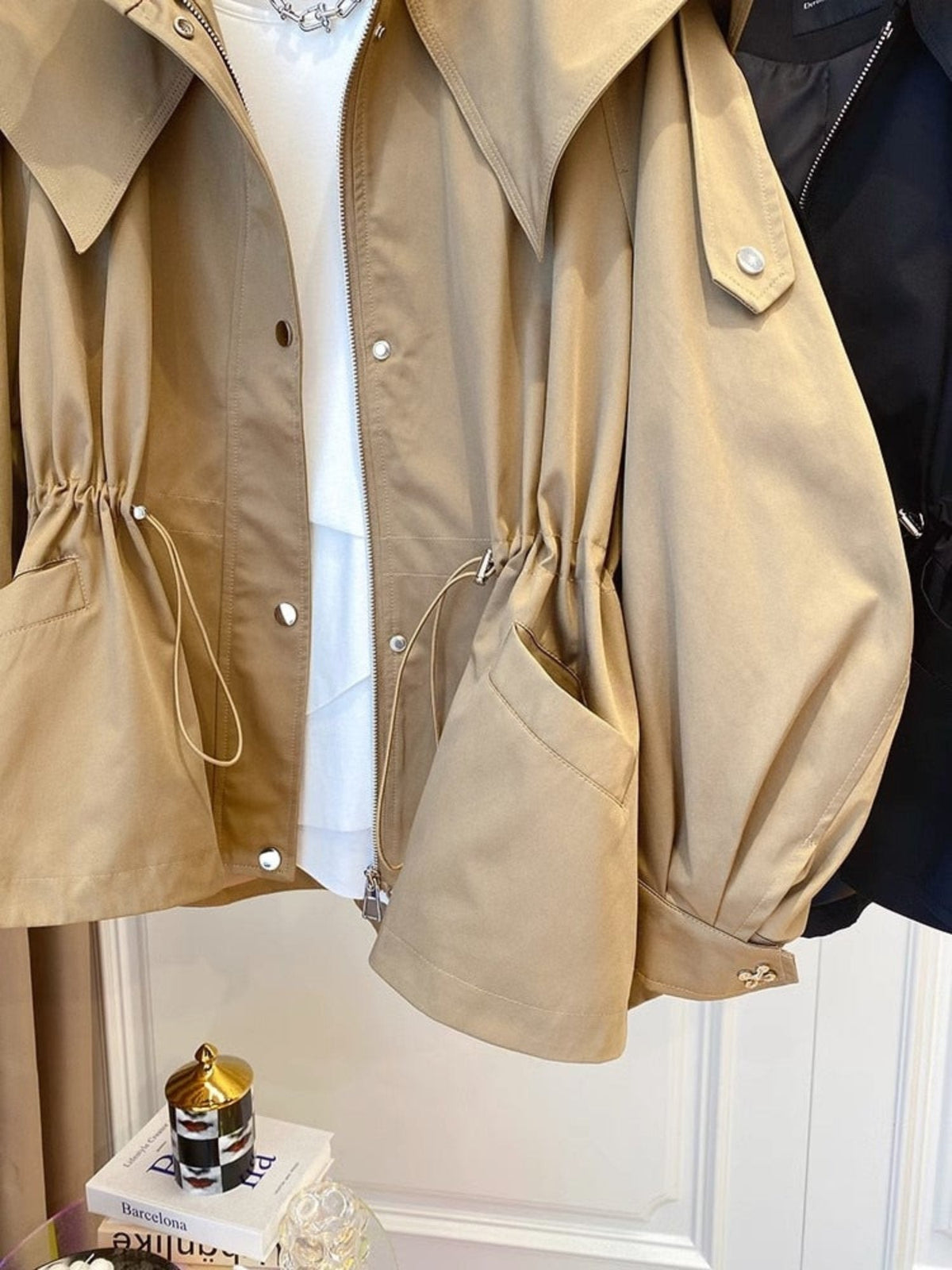 Close front detail of the jacket showing the gathered waist cords, snap-front closure, large patch pocket, and adjustable cuff tab.