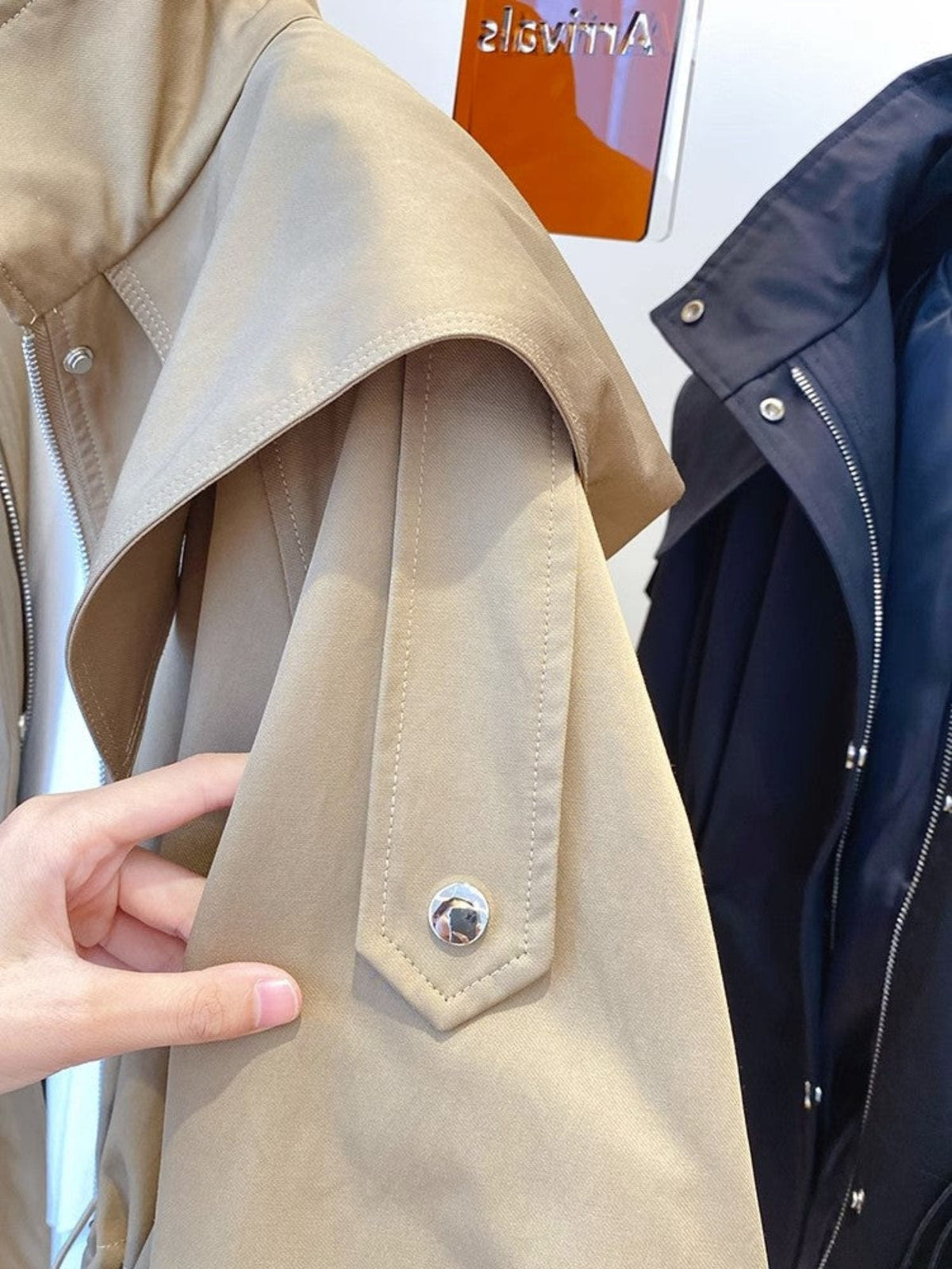 Close-up of the jacket's shoulder and sleeve, highlighting the layered shoulder flap, structured seam, and snap-fastened sleeve tab.