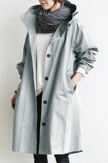 Light gray hooded longline coat worn with the hood raised, scarf, rolled sleeves, and hands placed in the side pockets.