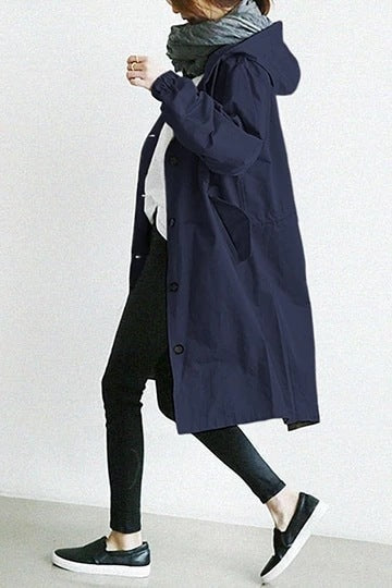 Navy hooded longline coat shown in side view while walking, revealing the hood, button closure, and angled pocket opening.