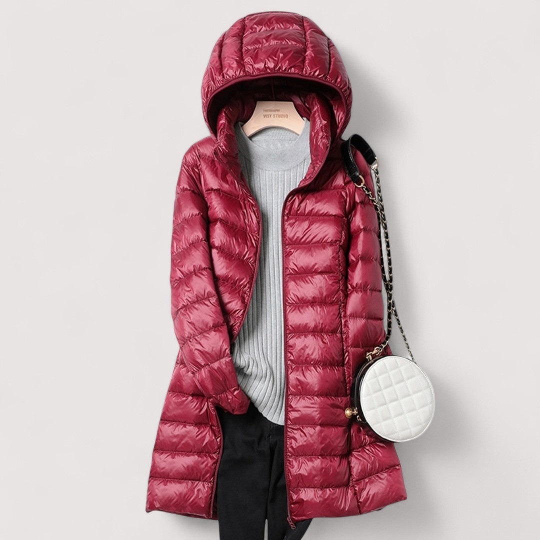 Burgundy hooded longline puffer jacket styled open over a grey knit top, with a round white shoulder bag.