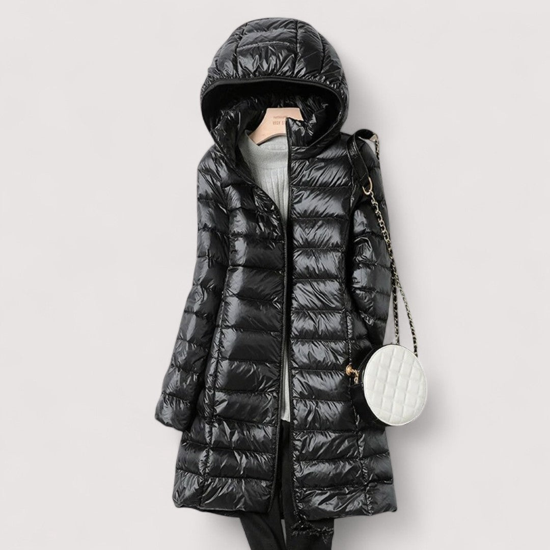 Black hooded longline puffer jacket styled over a light grey knit top, with a round white shoulder bag.