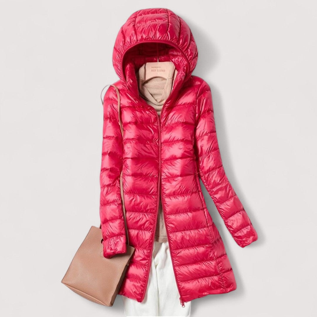 Red hooded longline puffer jacket shown open over a beige top and light trousers, with a tan shoulder bag.