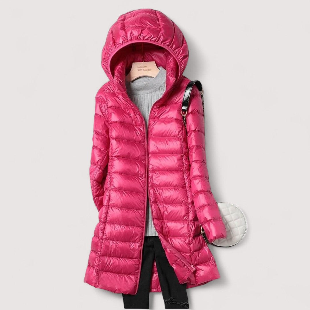 Fuchsia hooded longline puffer jacket styled open over a grey knit top and black trousers, with a round white bag.