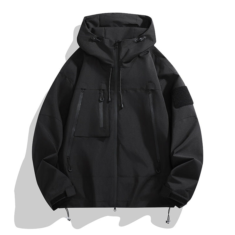 Black utility jacket showing its raised hood, full front zipper, flap-and-zip pocket arrangement, sleeve patch, and drawcord hem.