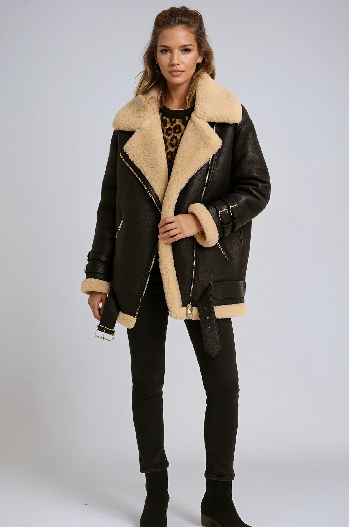 Black jacket featuring a wide plush collar, angled front zip, cuff accents, and a hanging buckle detail, paired with black pants and ankle boots.