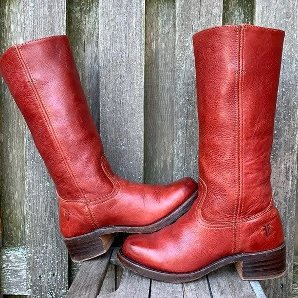 Red knee-high boots with rounded toes and dark stacked block heels posed against a weathered wooden backdrop.