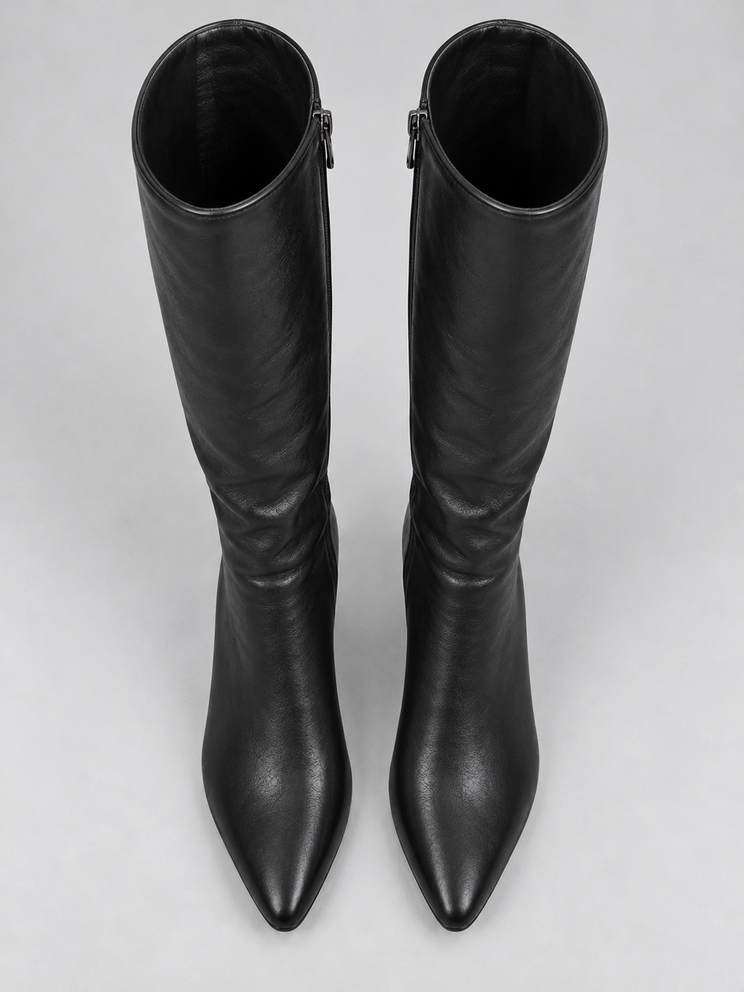 Top-down view of a pair of black knee-high boots showing their pointed toes, open shafts, and side zips near the upper edges.