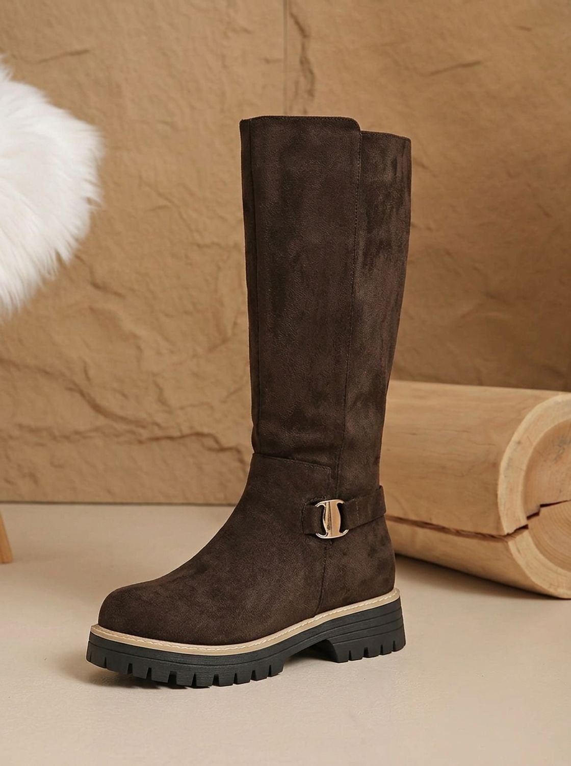 Single brown knee-high boot displayed upright, highlighting its tall shaft, decorative side buckle, low block heel, and lugged sole.