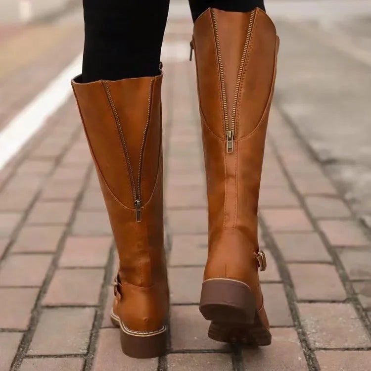 Tan knee-high boots viewed from the back while walking, with full-length rear zippers and low block heels visible.