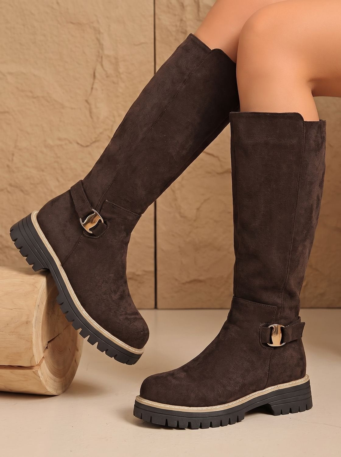 Brown knee-high boots shown in a crossed-leg pose, highlighting the side buckle details and contrasting rugged soles.
