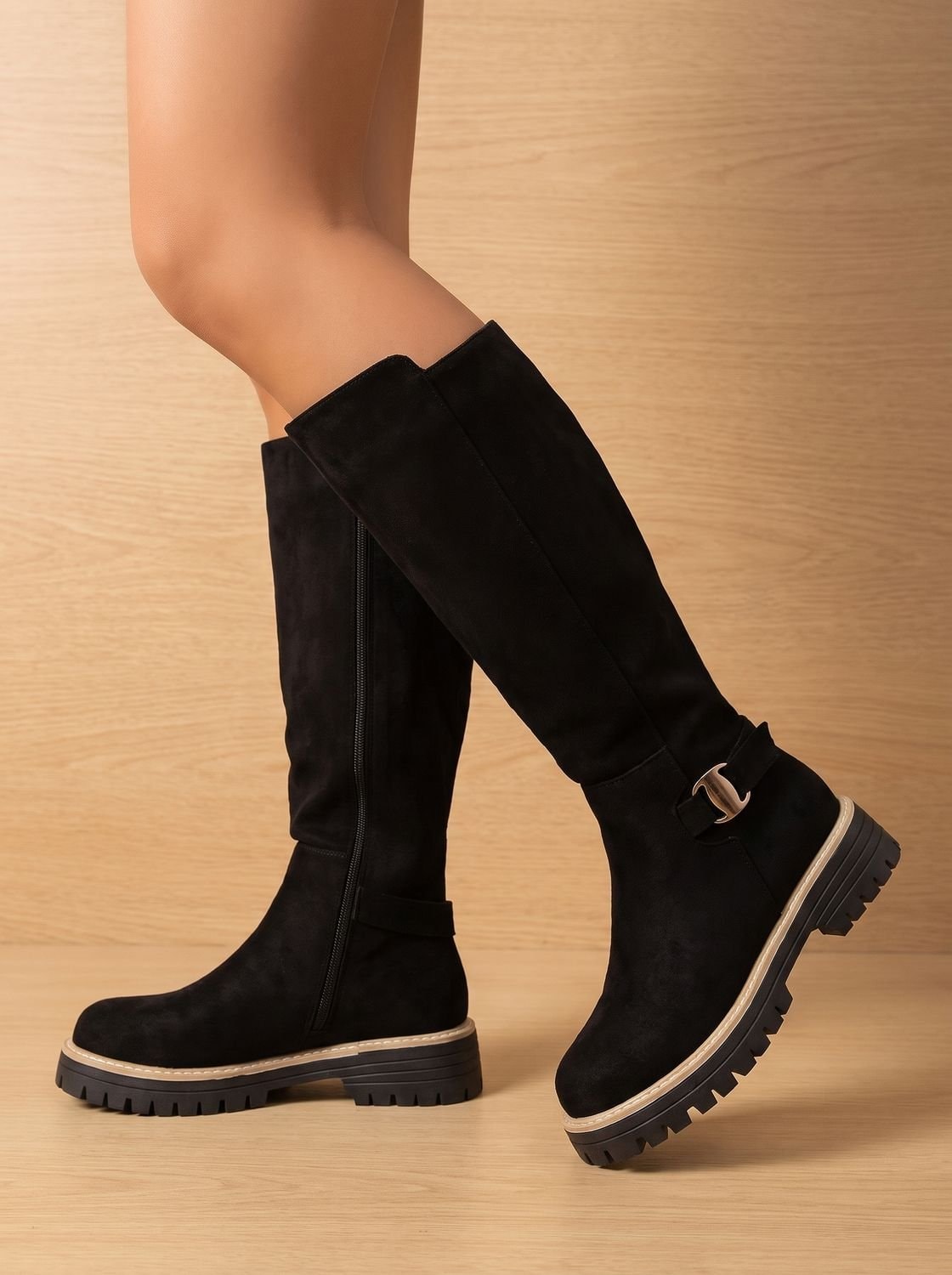 Black knee-high boots shown from the side, emphasizing the full-length shaft, side zipper, buckle strap, and raised treaded sole.