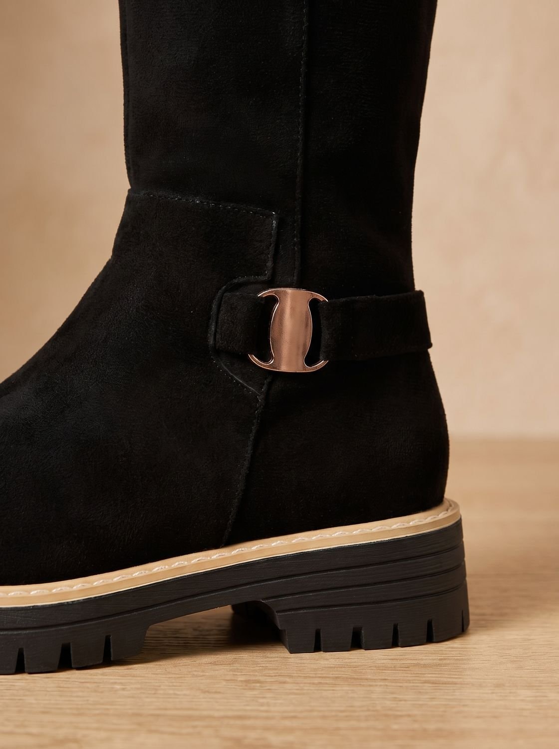 Close-up of a black boot’s decorative metal buckle strap, low block heel, layered sole edge, and rugged tread.