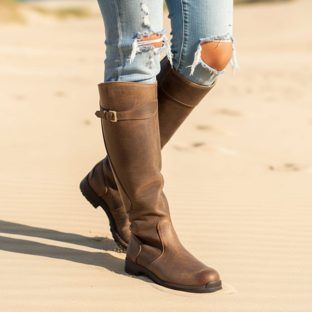 Woman wearing knee high boots with buckle detail paired with distressed jeans while standing outdoors._0
