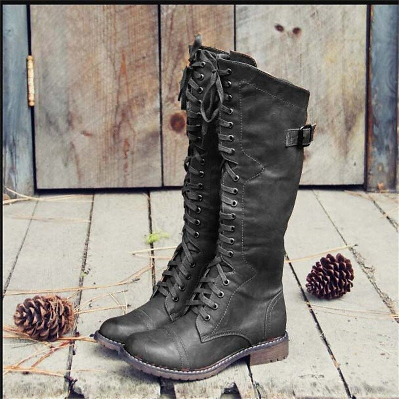 Black knee-high lace-up riding boots displayed from the side, highlighting the tall shaft, side buckle strap, rounded toe, and low block heel.