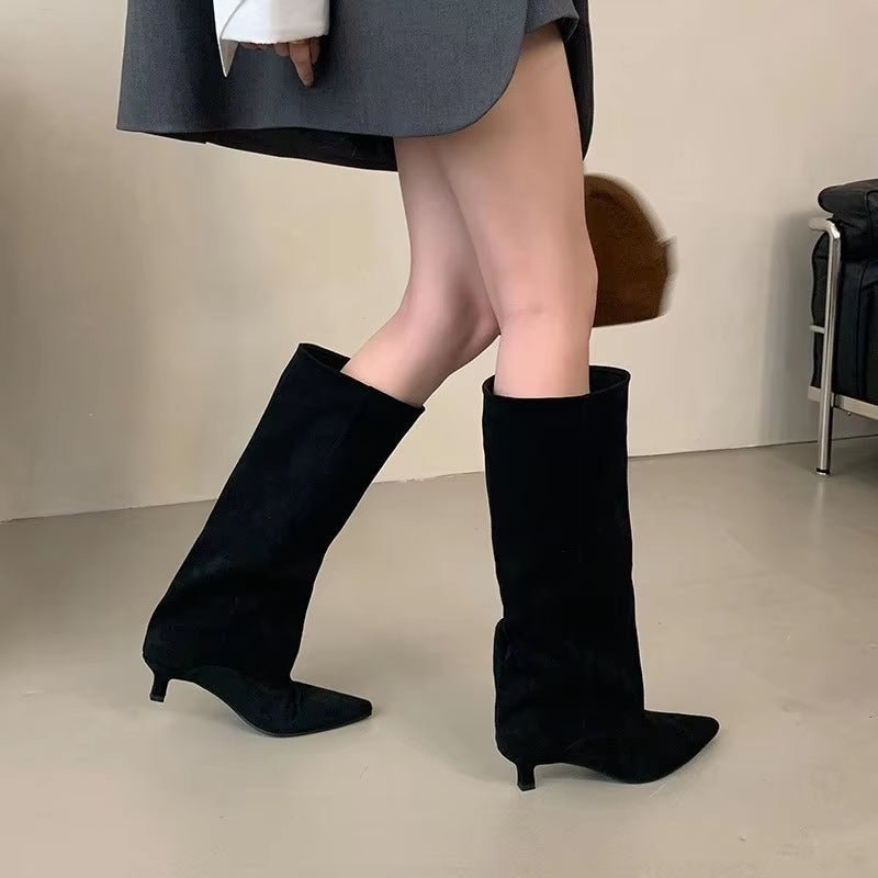 Black knee-high boots with pointed toes and low kitten heels styled beneath a gray skirt.
