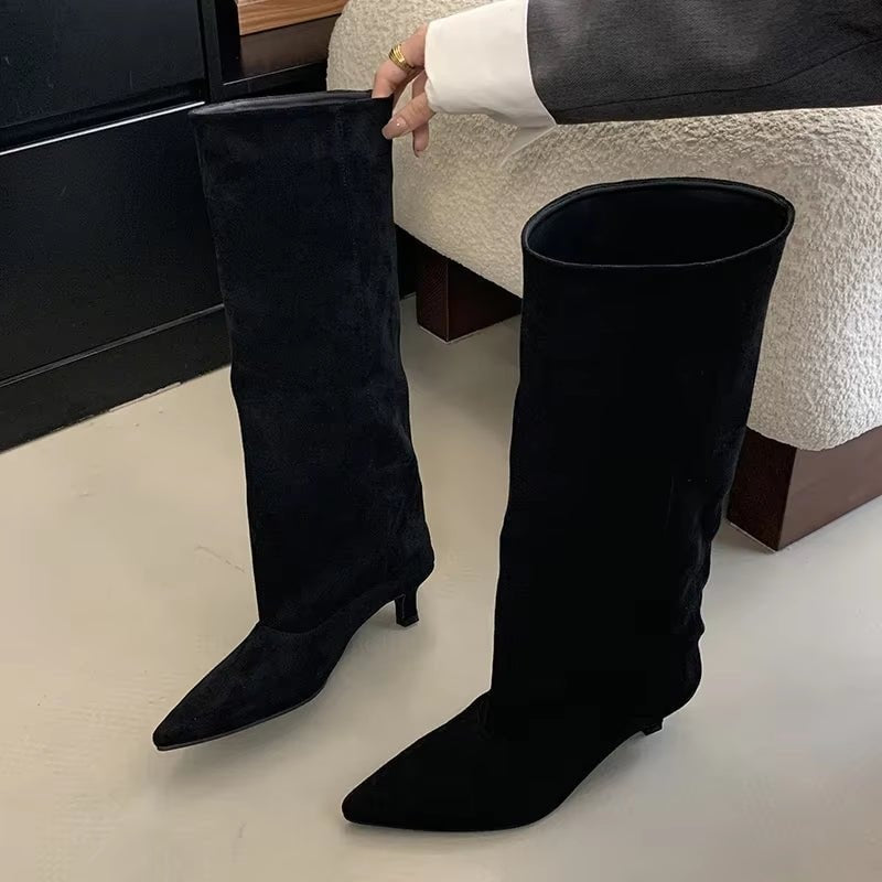 Pair of black knee-high pointed-toe boots displayed upright, showing their tall shaft and subtle heels.