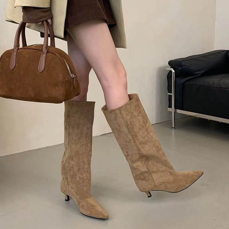 Tan knee-high pointed-toe boots with low kitten heels worn with a short skirt and handbag.