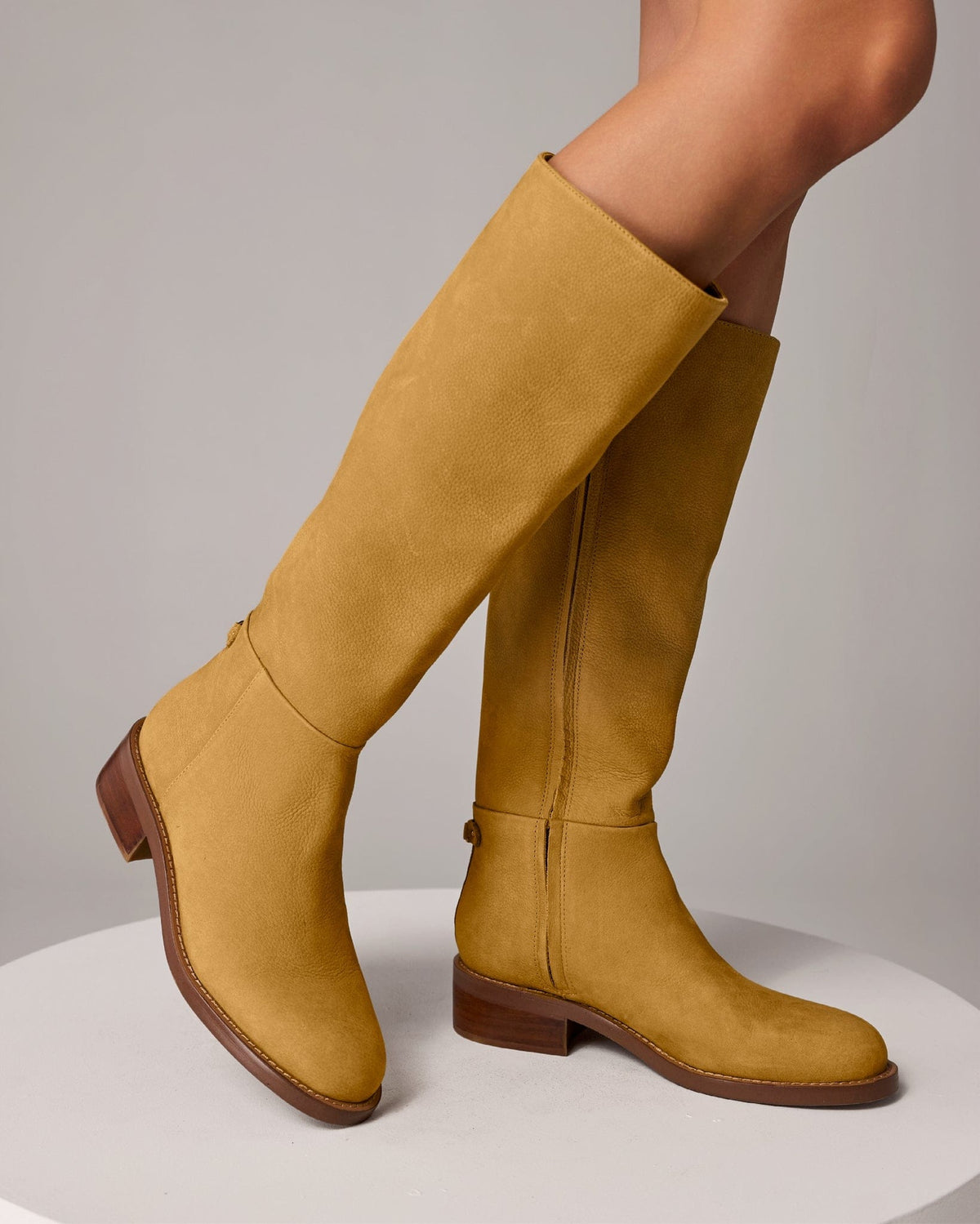 A knee-high riding boot with a low stacked heel and subtle back strap detail, shown in a warm neutral tone._1