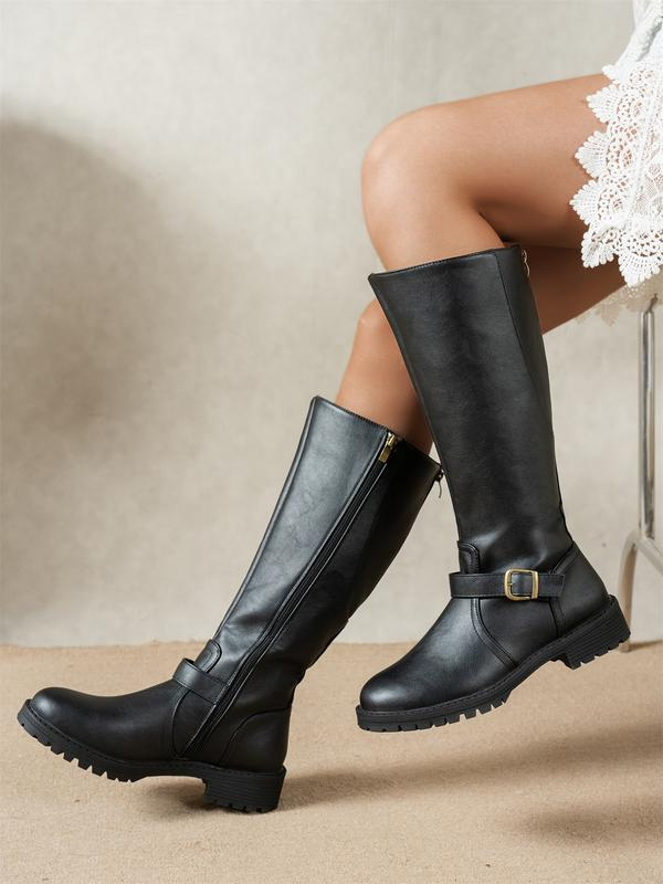 Black knee-high riding boots with side zips, ankle buckles, low heels, and rugged treaded soles shown on crossed legs.