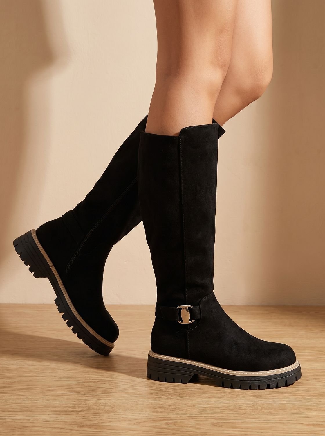 Black knee-high buckle boots shown in motion, highlighting the tall shaft, rounded toes, and rugged lug soles.